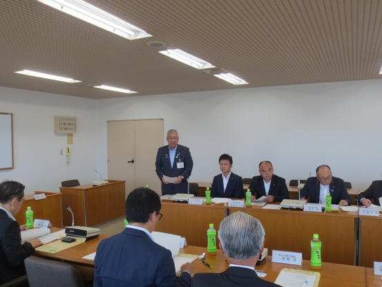 関係者が向かい合って座り、席から立ち上がった市長が挨拶を行っている様子の写真