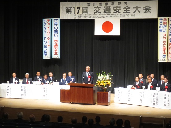 「第17回交通安全大会」と書かれた横断幕と国旗が飾られたステージ左右の席に関係者が座り、中央の演壇に立っている市長が挨拶を行っている様子の写真