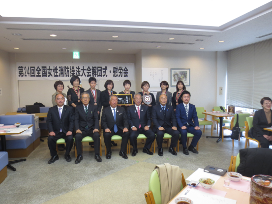 前列の椅子に市長を含め6名の男性が座り、後列にはメダルを掛け2つの盾を持って並んでいる8名の女性の記念写真