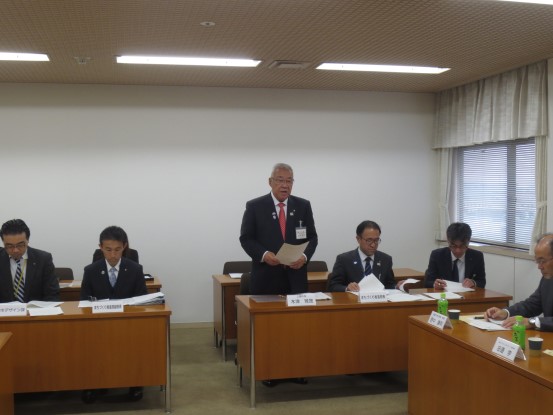 3名掛けの机の席から立ち上がり挨拶を行っている市長の写真
