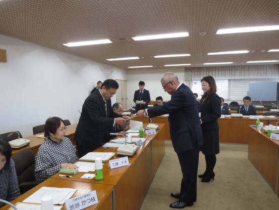 奥の席に担当者、左側の席に委員の方々が座り、奥から2番目の席から立ち上がった男性が市長から委嘱書を受け取っている様子の写真
