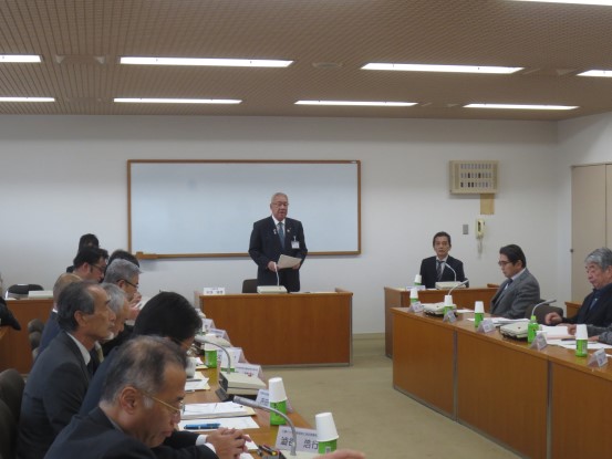 向かい合って設置された席に関係者や委員の方々が座り、ホワイトボードの前に設置された席から立ち上がり挨拶を行っている市長の写真