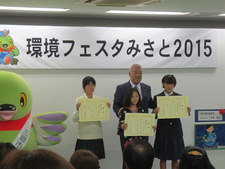 「環境フェスタみさと2015」と書かれた横断幕の前で市長と3名の女の子がそれぞれ賞状を持って並んで立っている写真