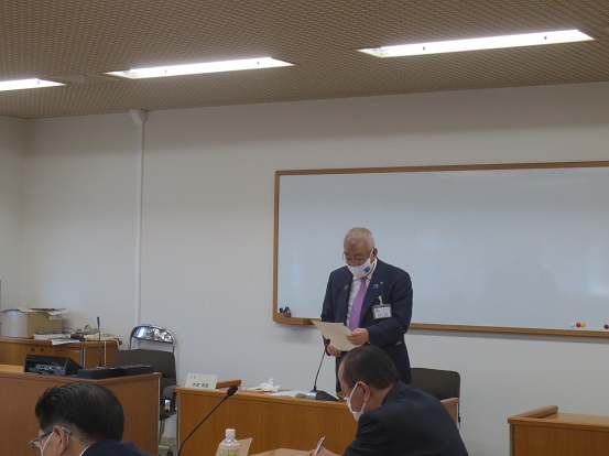 前方にホワイトボードがある会議室で、席を立って挨拶している三郷市長と、席に座って聞いている関係者の方々の写真
