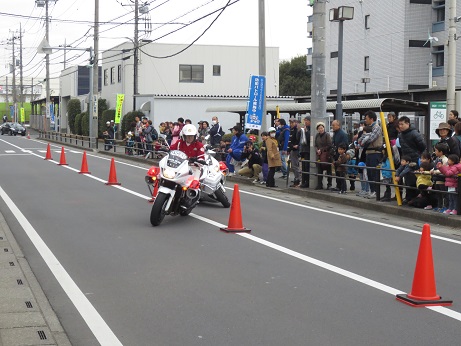 大勢の市民が見守るなか、間隔をあけて設置した三角コーンの間を白バイに乗った隊員が蛇行しながら実演を行っている様子の写真