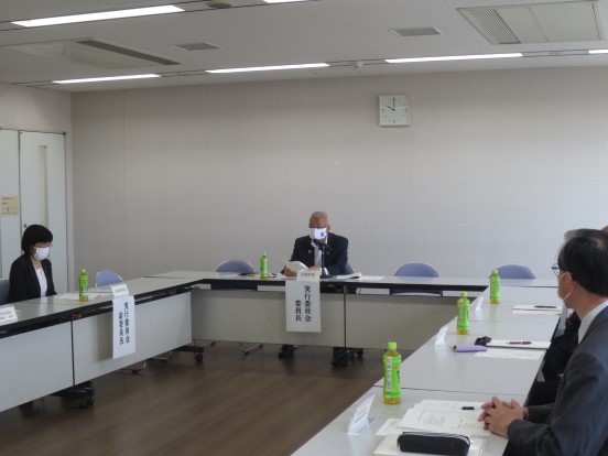 壁に時計が設置されている部屋で、席に座って挨拶をしている三郷市長と、席に座って聞いている3人の関係者の方々の写真