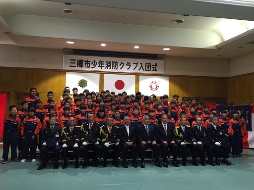 前列の椅子に市長を中央に9名の関係者が座り、後列に大勢の団員が並んで立っている記念写真