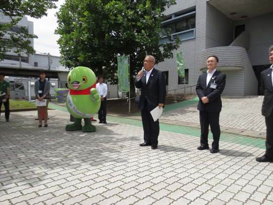 建物前のスペースでスーツ姿の市長がマイクを手に挨拶をしており、その周りで関係者やかいちゃんが立っている写真