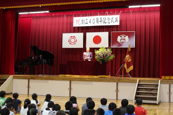 「祝 創立40周年記念式典」と書かれた横断幕に国旗に三郷市旗、校旗が飾られたステージの演台に立ち挨拶を行っている市長の祝辞の様子の写真