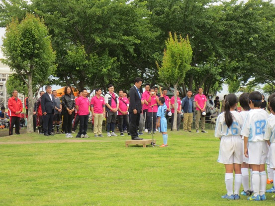 芝生の広がる広場で、1名の男児が台の上に立つ男性に向かって選手宣誓をしている様子の写真