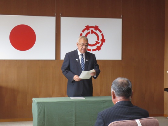 スーツ姿の市長が、手元の資料を見ながら話をしており、椅子に座る関係者が市長の方を向いている写真