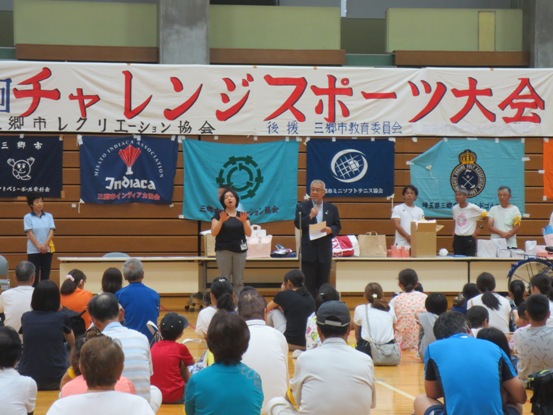壁に「チャレンジスポーツ大会」の横断幕が貼られた体育館で、床に座っている参加者たちの正面に立って話をしている市長の写真
