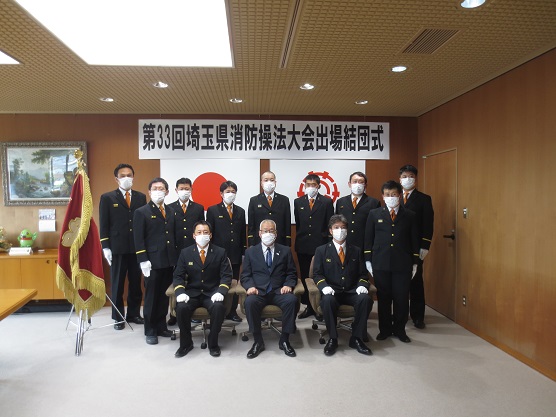 「第33回埼玉県消防操法大会出場結団式」に参加された黒い制服を着た方々と三郷市長が一緒に記念撮影をしている写真