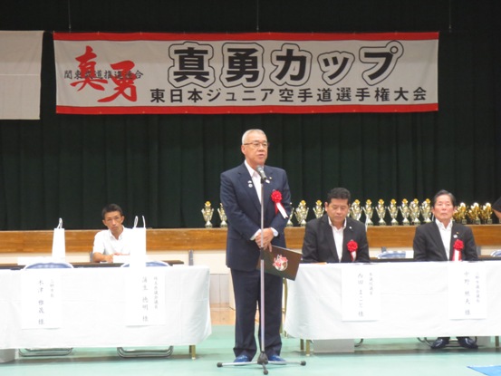 「真勇カップ東日本ジュニア空手道選手権大会」の横断幕が設置された会場で、胸章を着けた市長が挨拶をしている写真