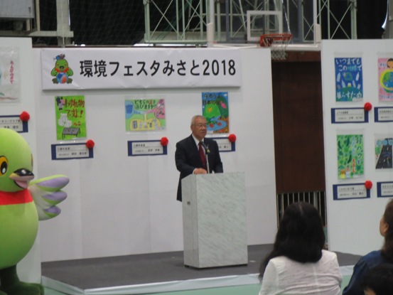 「環境フェスタ2018」のボードや、絵の作品が数多く展示されている会場で、演壇に立って話をしている市長の写真