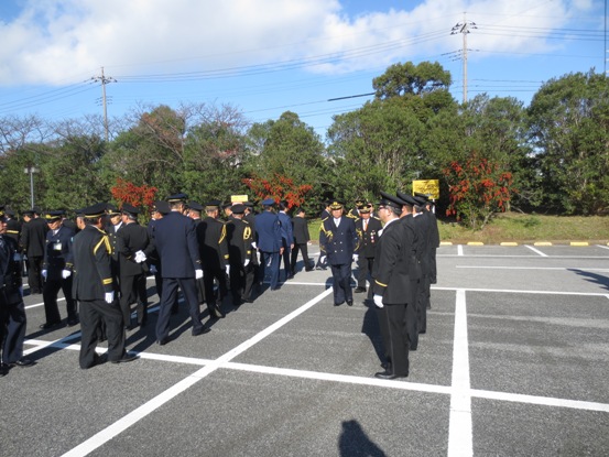 白線が引かれている駐車場で、制服を着用した参加者が一列に並んで行動している「人員・服装・規律」点検の様子の写真