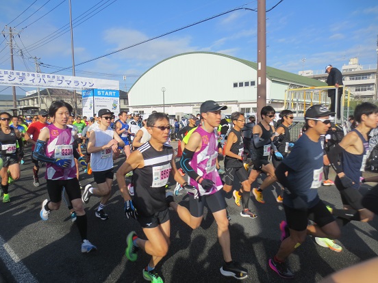 ランニングウェアを着たたくさんのランナーが、ハーフの部のスタート地点を出発している写真