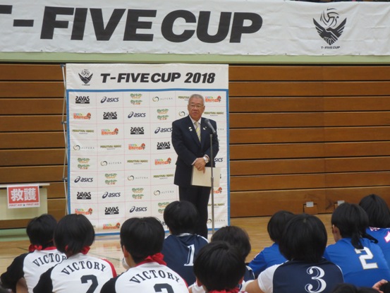体育館にたくさんの参加者が並んで座っているなか、正面の市長がマイク台の前に立って挨拶をしている写真