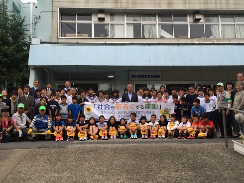 校舎の前に地域の方々と小中学生が集まり、市長を中央に「社会を明るくする運動」と書かれた横断幕を持って並んでいる集合写真