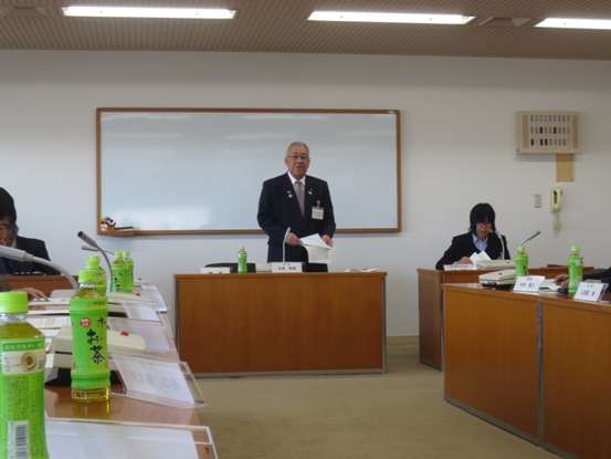 向かい合わせに設置された長テーブルに資料や飲み物が用意された部屋で、正面中央に立つ市長が立って挨拶をしている写真