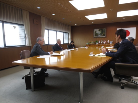 大きなテーブルが設置されている部屋で、数名の関係者が向かい合わせに着席しており、窓側の真ん中の席に市長が座っている写真