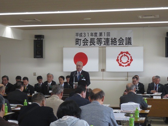 「平成31年度第1回町会長等連絡会議」の紙が貼られた部屋で、多くの関係者たちが椅子に着席しているなか、正面に立つ市長がマイク台の前で挨拶をしている写真