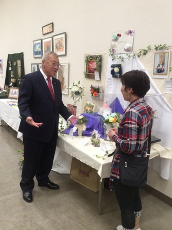 花で造られた作品が展示されている前で市長と女性が向かい合って話をしている写真