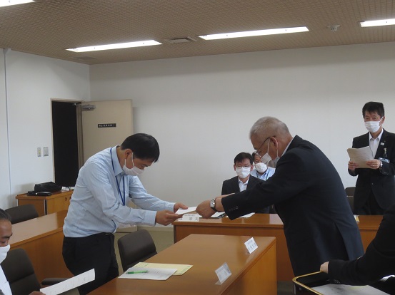 関係者たちが椅子に着席しているなか、1名の男性が市長から委嘱書の交付をうけている写真