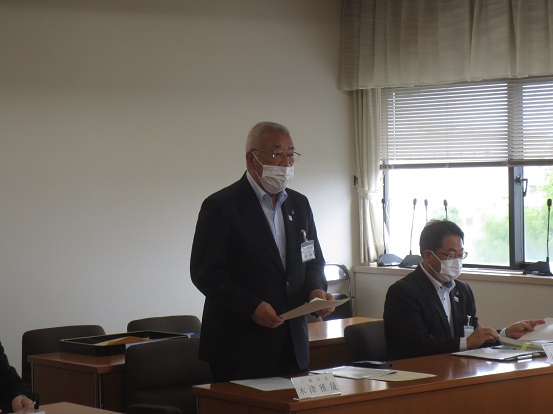 手元の長テーブルに資料を置いて起立して挨拶をしている市長の写真