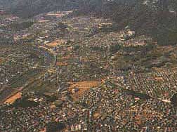 山の麓に多くの住宅が建ち並び、左側にカーブを描いて流れる川のある奈良県生駒郡三郷町の航空写真