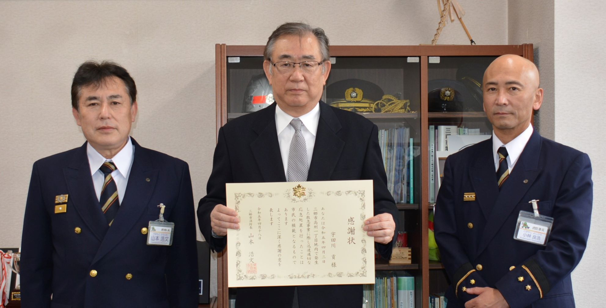 宇田川貢さんが感謝状を持っており、両サイドに消防長と消防署長が横一列に並んで記念撮影をしている写真