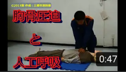 隊員がマネキンの心臓付近に上から真っ直ぐ両手を下して胸骨圧迫を行っている写真（胸骨圧迫・人工呼吸～心肺蘇生法手順【Ｇ2015版 三郷市消防署作成】（YouTubeのサイトへリンク））
