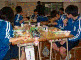 机をくっつけてジャージ姿の生徒達が給食を食べている写真