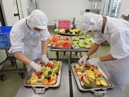 給食着をきた2名が一人ずつフルーツを器に盛り付けしている写真
