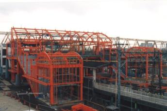 屋根部分がアーチ状の赤い鉄骨が組まれた建設途中の新三郷駅舎の写真