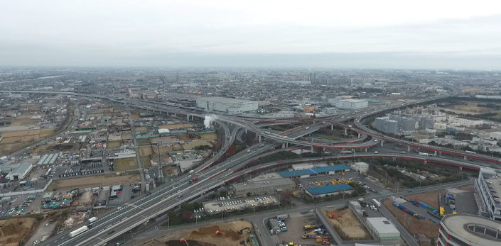 カーブや直線の道路が上下で立体交差しているインターチェンジを中心に高速道路が四方に伸びて街中を通っている写真