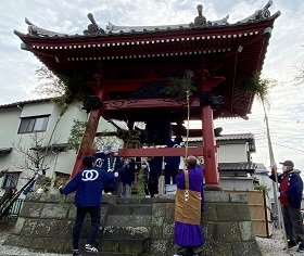 鐘楼堂の屋根を参加者やお坊さんが笹竹の先に葉を付けたものですす払いを行っている様子の写真