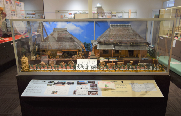 茅葺屋根の主家と左側に茅葺屋根の厩（作業所兼馬屋）、多数多様の農具のミニチュアの展示物の写真