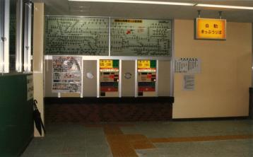 券売機が2つ並んでおり、料金表が頭上に設置してある新三郷駅開業当時の切符売り場の写真