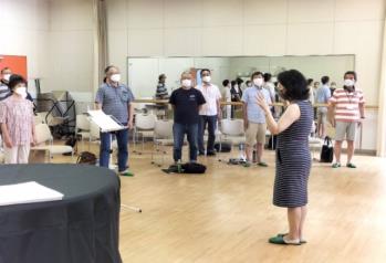 ピアノが置かれた室内で、扇状に並んだ椅子の前に立ち講師の方を向く三郷第九合唱団の団員たちと中央で指導するボイストレーニング講師の女性の写真