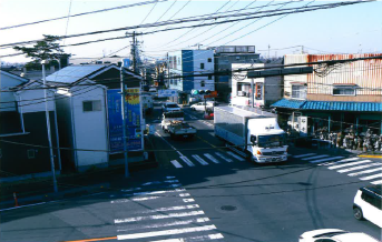 地名表示板が付けられた信号機が設置され、トラックや車が行きかっている交差点を上から撮ったカラー写真