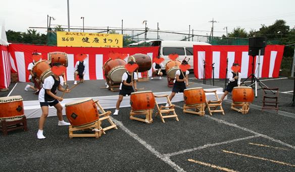 紅白幕が張られた健康まつりのステージで和太鼓を叩く二龍太鼓クラブのメンバーの写真