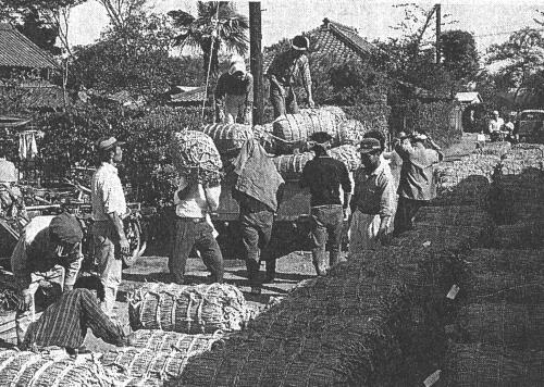 たくさんの男性が、俵に入ったお米を車に積み込み出荷準備をしている白黒写真