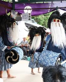 黒い頭に白のひげが特徴の獅子舞を被った3人の人が、腰に太鼓をつけて演舞している写真