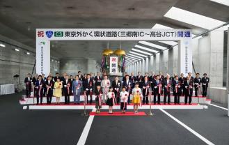 くす玉が割れ、口角のテープカットが行われて、開通式典に参加したたくさんの関係者と前列に並んでいる4名の子ども達が並んでいる念撮影の写真