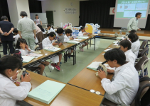 長机の席に座り顕微鏡を覗いている子ども達の様子を写した写真