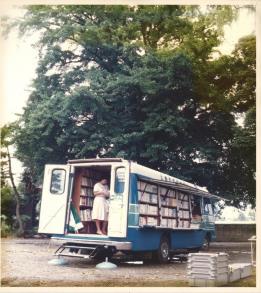 たくさんの本が格納されている移動図書館車「ふれあい号」と、車に乗って本を見ている女性の写真