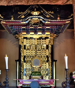 左右対称に灯りが灯されたロウソクがあり、丸い御守鏡が赤い欄間の上に設置されている黒や金色で宝飾された厨子の外観写真