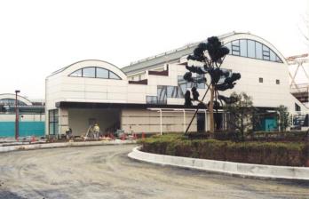 白を基調とした建物で、作業員の方が測量をしている完成間近の新三郷駅の写真