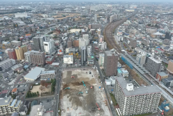 奥に向かって緩やかなカーブになっている線路を挟んで沢山のビルやマンションが建ち並ぶ三郷駅を上空から撮影した写真